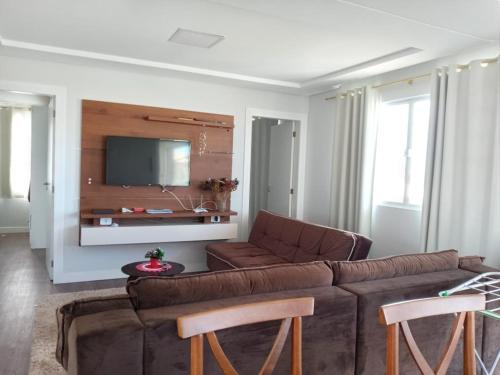 a living room with a brown couch and a flat screen tv at Apartamento Ponta do Papagaio - Com Varanda in Palhoça