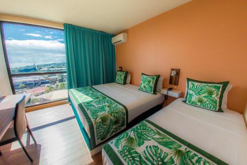 two beds in a room with a large window at Tahiti Airport Motel in Faaa