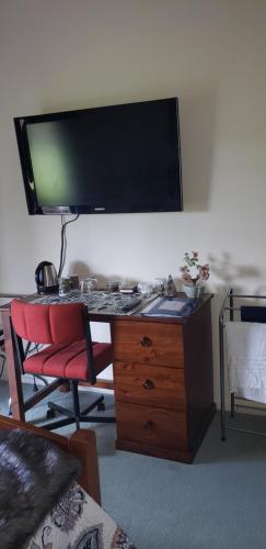 uma secretária com uma televisão numa parede com uma cadeira vermelha em Ballymena em Carterton