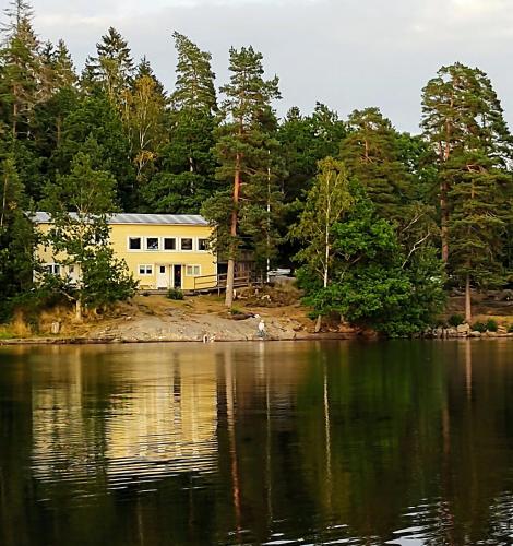 a yellow building on the shore of a lake at Vårhaga Vandrarhem in Sjuntorp