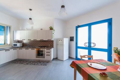 una cucina con armadi bianchi, tavolo e frigorifero di B&B "Perla del Sud" a San Vito lo Capo