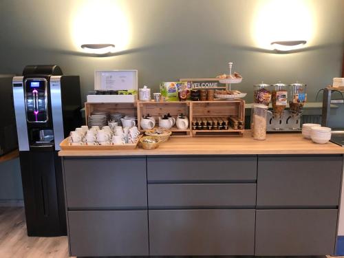 a kitchen with a counter with cups and a refrigerator at Logis L'Hôtel D'Arc in Arc-sur-Tille