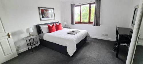 a bedroom with a bed with red pillows and a desk at Levenhowe Holiday Apartment in Balloch