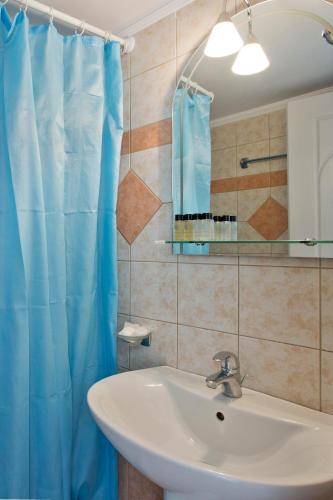 a bathroom with a sink and a blue shower curtain at Santorini Med Homes - Sunday Apartment in Mesaria