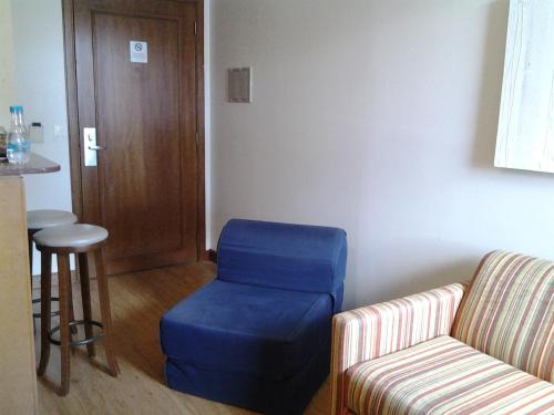 a room with a blue ottoman and a chair and a stool at Flat em Gramado in Gramado