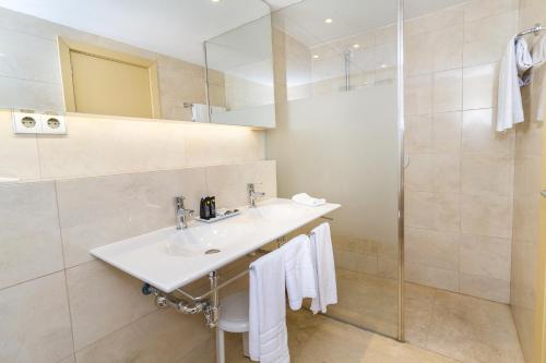
a bathroom with a sink, mirror, and towel rack at Eix Platja Daurada Hotel & SPA in Can Picafort
