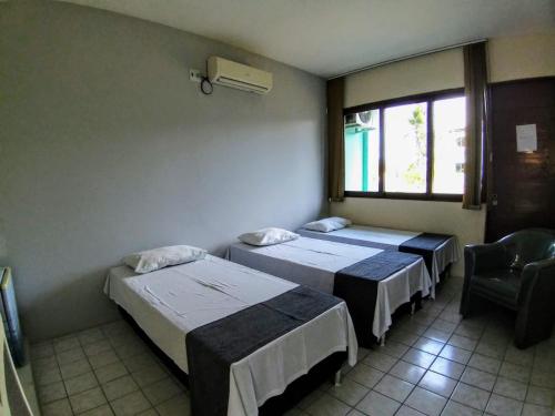 a room with two beds and a chair and a window at Hotel de Trânsito da PM-PE in Olinda