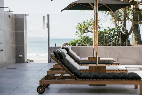 a row of lounge chairs with an umbrella and the ocean at On The Beach Noosa Resort in Noosa Heads