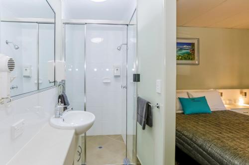 a bathroom with a shower and a sink and a bed at Matilda Motel in Bundaberg