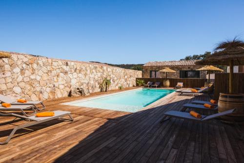 une piscine avec des chaises longues et un mur en pierre dans l'établissement Petra d'Oro Villa Palombaggia, à Porto-Vecchio