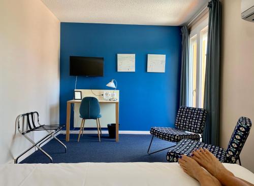 a bedroom with a blue wall and a desk and chairs at Amerique Hotel Palavas - Piscine & Parking - Plage in Palavas-les-Flots
