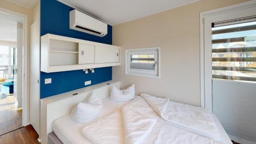 een slaapkamer met een bed met witte lakens en een blauwe muur bij Floating Village Brombachsee in Ramsberg