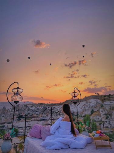 a woman sitting on a bed watching kites fly in the sky at Traveller's Cave Hotel in Goreme