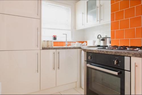 una cucina con armadi bianchi e una parete di piastrelle arancioni di 03 Bedroom Apartment-Self Check in a Londra