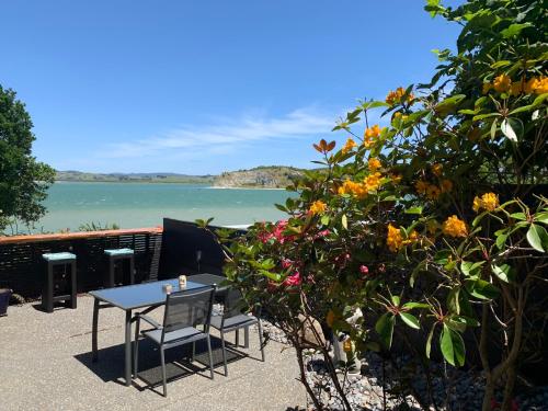 a table and chairs on the beach with the ocean at Beach Lane Apartment in Whangarei