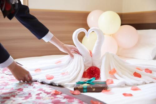 a person cutting a wedding cake with swans on a bed at Hot Spring Osaka Hinode Hotel Nipponbashi in Osaka