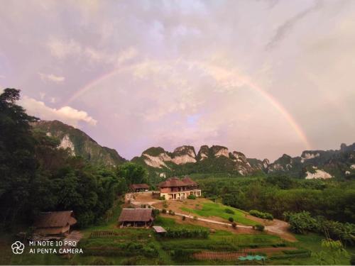 a rainbow over a house in a field with mountains at Billion Views Khaosok Homestay in Khao Sok