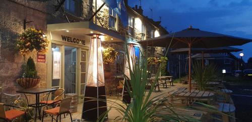 a restaurant with tables and umbrellas in front of a building at The Queen Catherine Hotel in Osmotherley