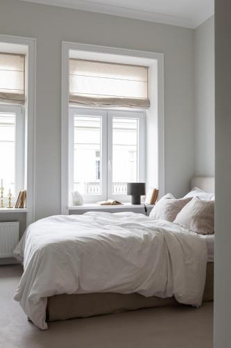 a white bedroom with a large bed and two windows at Lwowska Studios - STAYINWARSAW in Warsaw