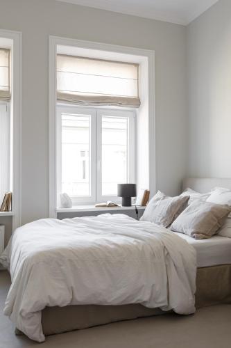 a white bedroom with a large bed and two windows at Lwowska Studios - STAYINWARSAW in Warsaw