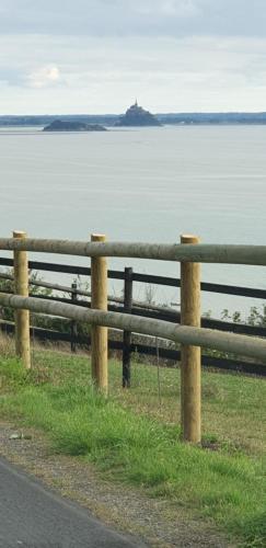 a fence on the side of a road near the water at Chez Jollyjune, à moins d'une heure du Mont Saint Michel in Champeaux