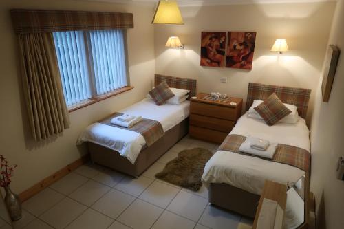 two beds in a small room with two windows at Corunna Cottage in Inverness