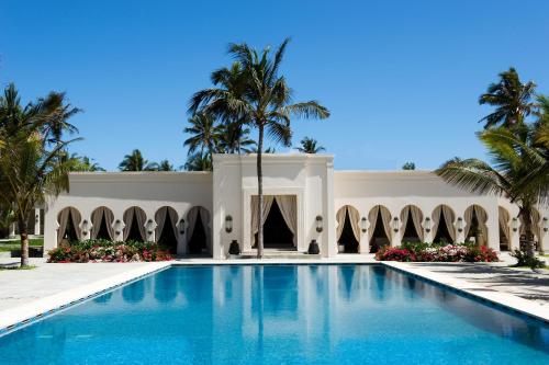 a swimming pool in front of a building with palm trees at Baraza Resort and Spa Zanzibar in Bwejuu