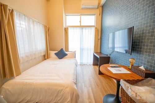 a bedroom with a bed and a table and a tv at Hotel Tomas Asahibashi Station in Naha