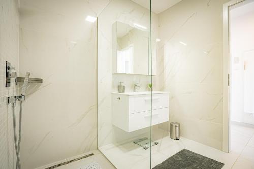 a white bathroom with a glass shower and a sink at Panoráma Apartman Tiszafüred in Tiszafüred