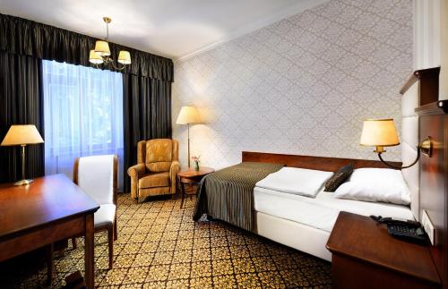 a hotel room with a bed, chair, and nightstand at Grand Hotel Praha in Vysoké Tatry