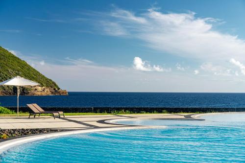 a swimming pool with a bench and the ocean at Terceira Mar Hotel in Angra do Heroísmo