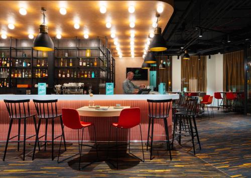 a bar with red chairs and a man standing at a counter at Holiday Inn Gdansk - City Centre by IHG in Gdańsk