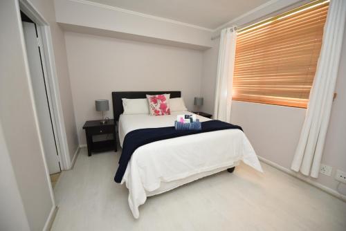 a white bedroom with a bed and a window at The Island Club Apartment in Cape Town