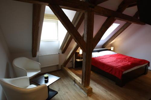 a attic bedroom with a red bed and two white chairs at Hotel Peregrin in Český Krumlov