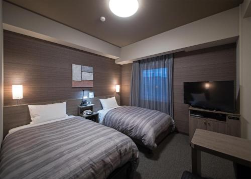 a hotel room with two beds and a flat screen tv at Hotel Route-Inn Hamada Ekimae in Hamada