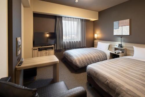 a hotel room with two beds and a television at Hotel Route-Inn Yahaba in Yahaba