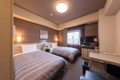 a hotel room with two beds and a flat screen tv at Hotel Route-Inn Kurashiki Mizushima in Kurashiki