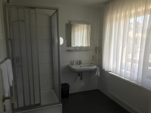 a bathroom with a sink and a shower with a mirror at Rixbecker Alpen - Hotel Koch in Lippstadt