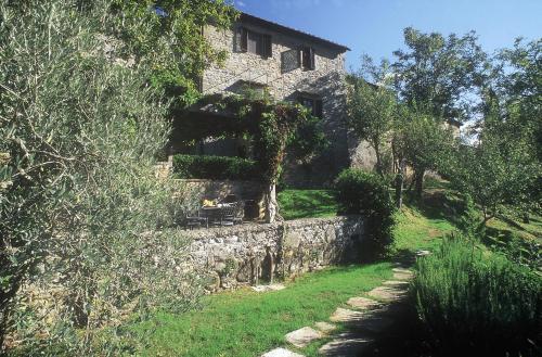 an old stone house with a stone wall and trees at Castello di Volpaia in Radda in Chianti