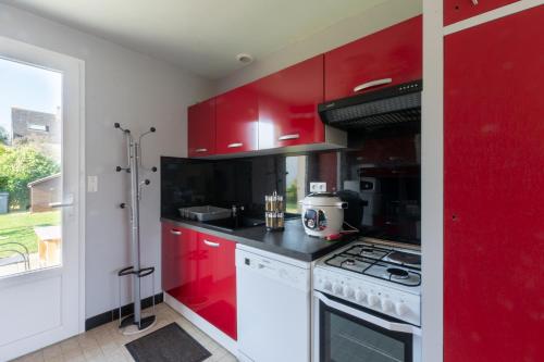 La cuisine est équipée de placards rouges et d'un four avec plaques de cuisson. dans l'établissement La Petite Isle - Maison et jardin - plage à 200 m, à Barneville-Carteret