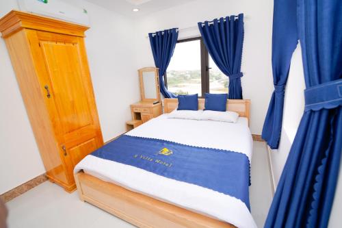 a bedroom with a bed with blue curtains and a window at S Villa Hotel in Da Thanh