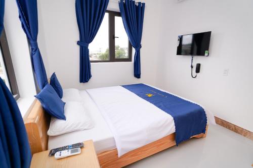 a bedroom with a bed with blue curtains and a tv at S Villa Hotel in Da Thanh