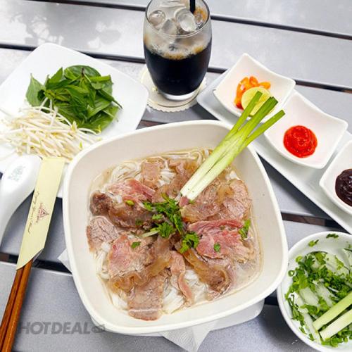 a table with a bowl of noodles and a drink at Vilion Boutique Hotel Ben Thanh in Ho Chi Minh City