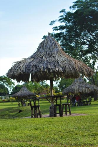 a group of picnic tables with a straw umbrella at Hotel Brisas La Gaviota Mariquit-Tolima in Mariquita