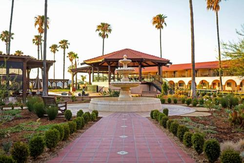 a fountain in a park with a building and palm trees at Hotel Mission De Oro in Santa Nella Village