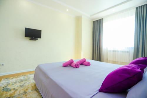 Schlafzimmer mit einem Bett mit lila Kissen und einem TV in der Unterkunft Уютная квартира в ЖК Bir Group Актобе in Aqtöbe