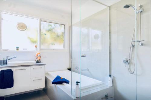 a white bathroom with a shower and a sink at By The Beach Frankston in Frankston