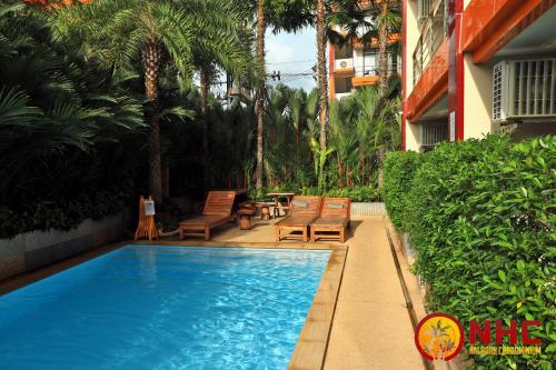 a swimming pool next to a building with chairs and trees at Nai Harn Condominium in Nai Harn Beach