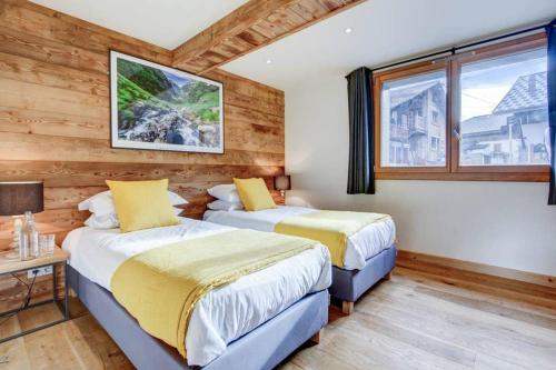 two beds in a room with wooden walls and windows at Chalet La Petite Grange in Morzine