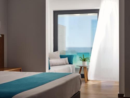 a bedroom with a bed and a chair and a window at Cavo Orient Beach Hotel & Suites in Tragaki